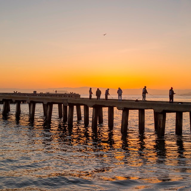 People fishing on torpedo wharf at sunset