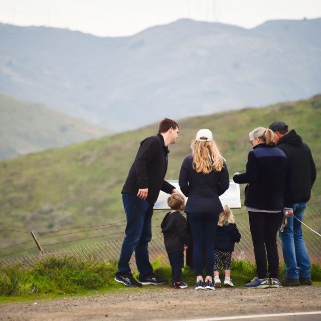 Family crowds around wayside talking and pointing to its text