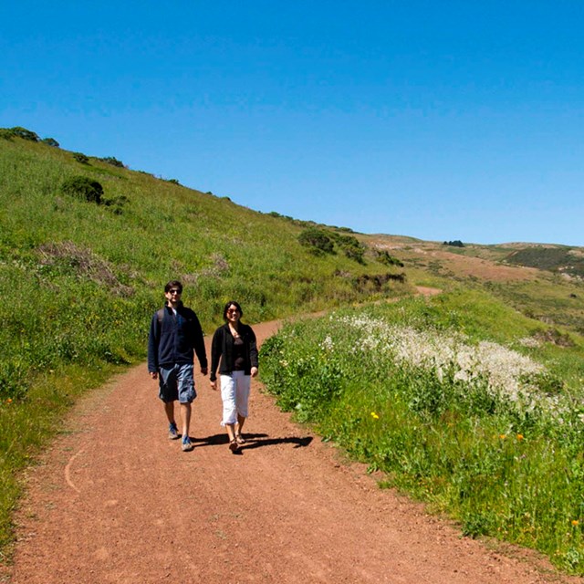 Visitors hike a path through the green and grassy coastal chapparal of Gerbode Valley