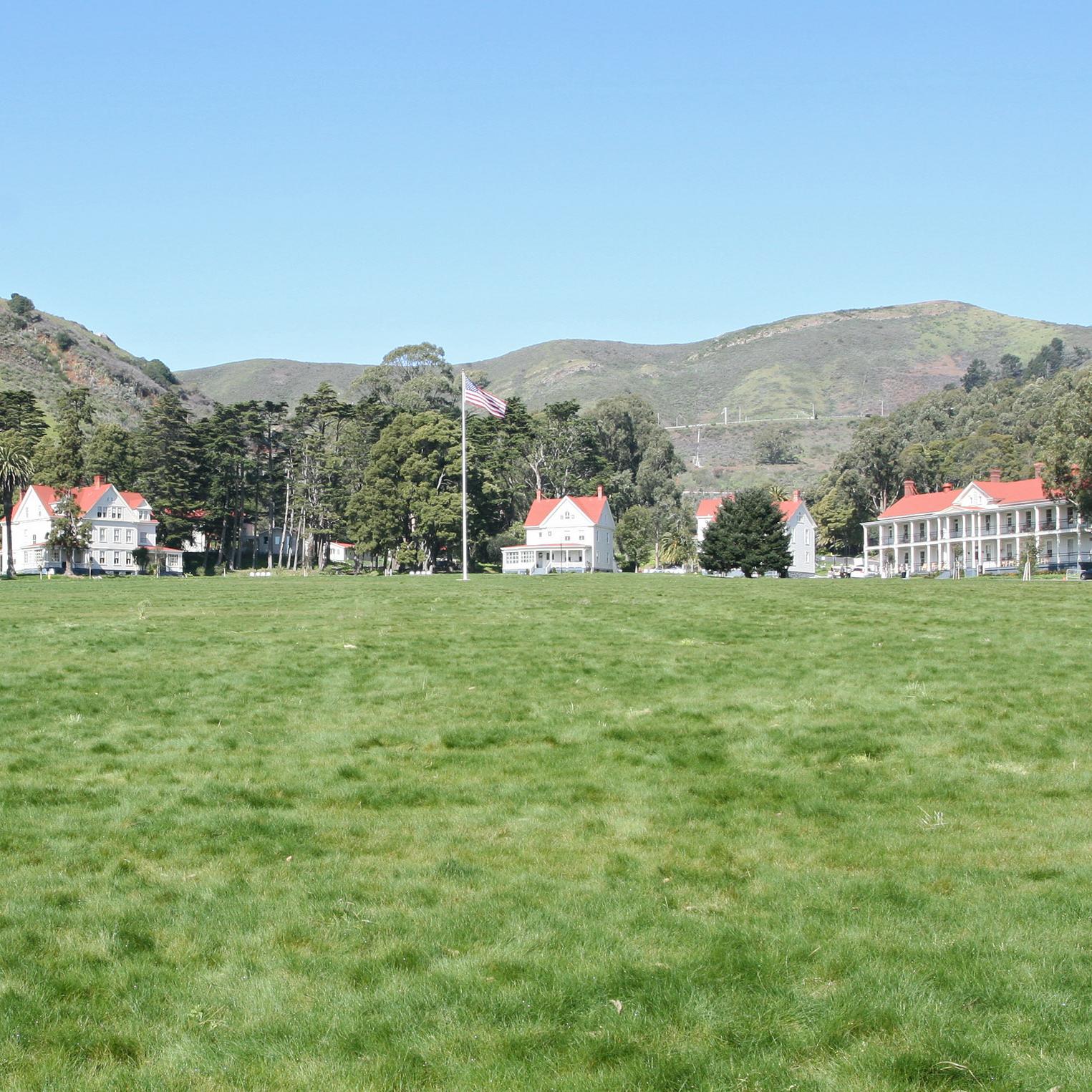 Grassy lawn of restored parade ground with restored buildings and flagpole behind