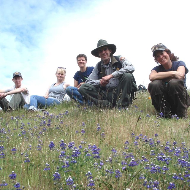 Natural resources staff and volunteers pause for a photo on a flower-filled hillside.