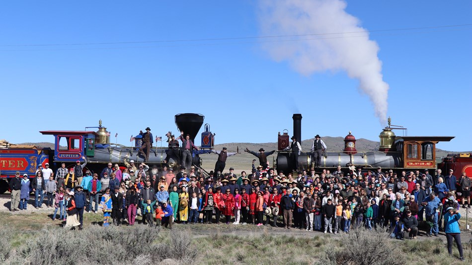 People gather around the two locomotives and recreate the champagne photograph. 