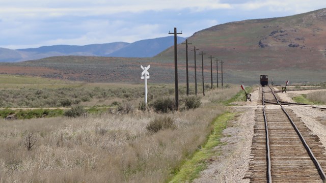 Railroad Tracks with a mountain and locomotive in the background.