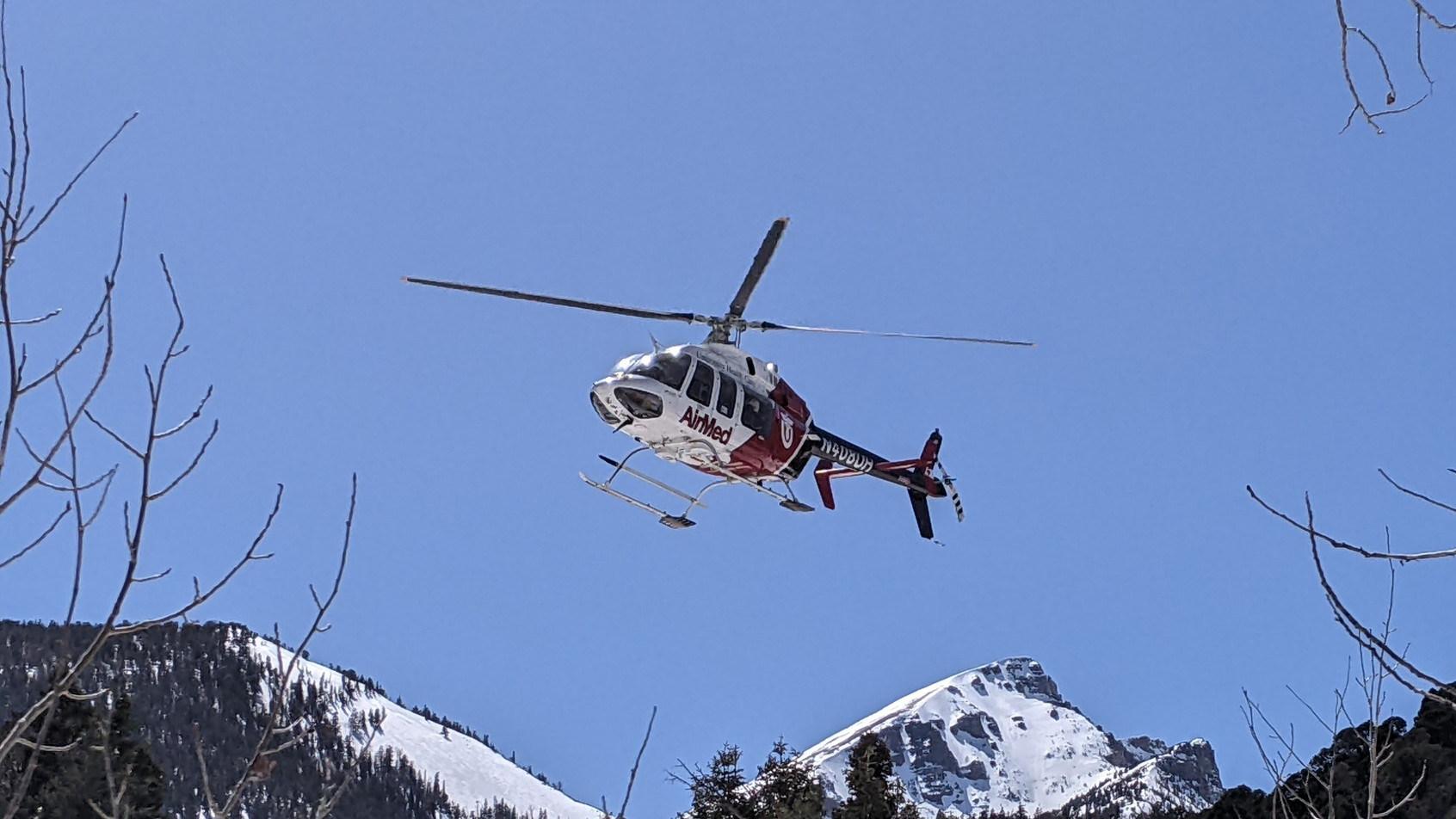 A red and white helicopter flies above a canyon with clear blue skies above