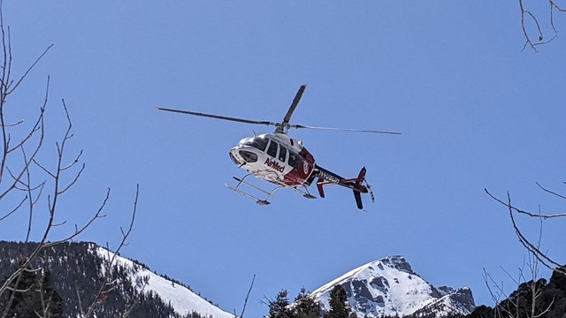 A red and white helicopter flies above a canyon with clear blue skies above