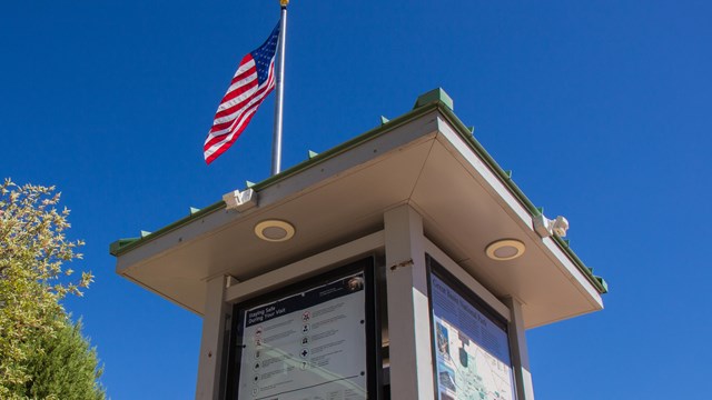 An information board standing below a blue sky and American flag
