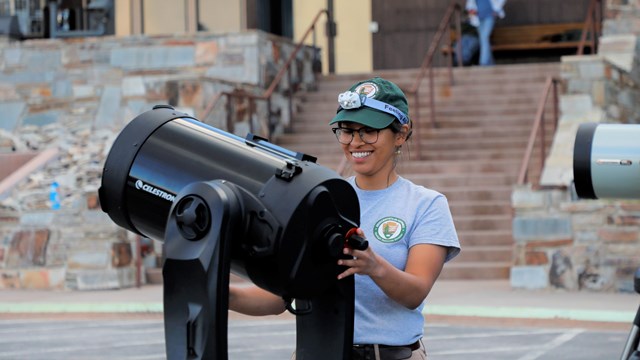 Intern setting up black telescope in front of Lehman Caves Visitor Center.