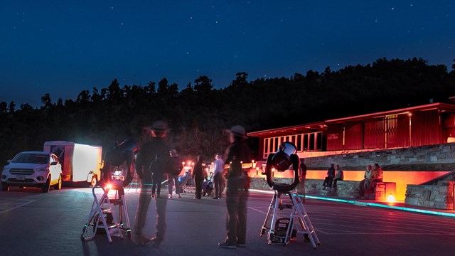 Telescopes set up in the parking lot with red lit visitor center in background