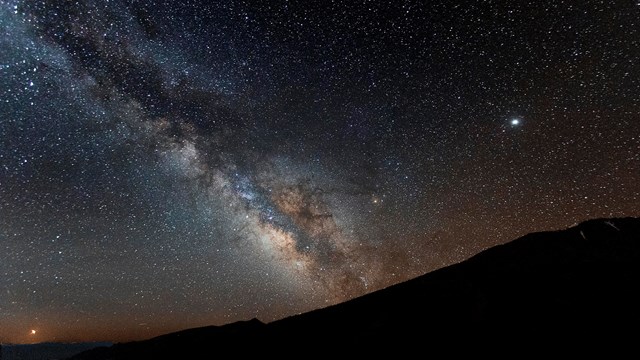Milky way over a red lit Lehman Caves Visitor Center and mountain ridge
