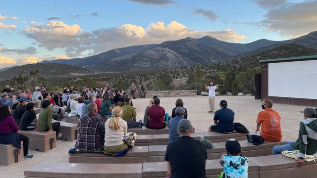 Guest speaker in a white shirt talking to a crowd of people.