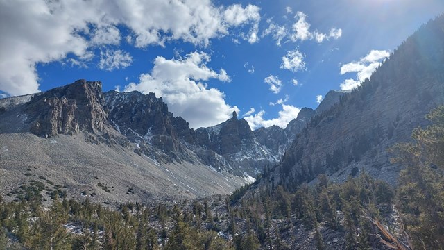 The sun glows in a blue sky above sharp mountain peaks surrounding a rocky valley