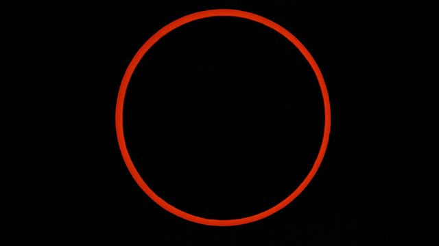 A black circle in the center of the image is surrounded by a thin glow of warm orange.