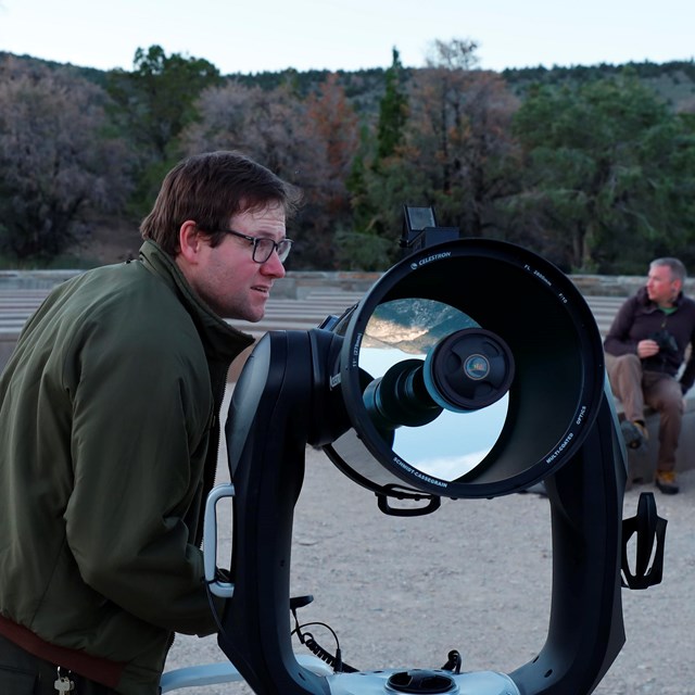 A ranger peers into the distance while preparing a telescope during dusk