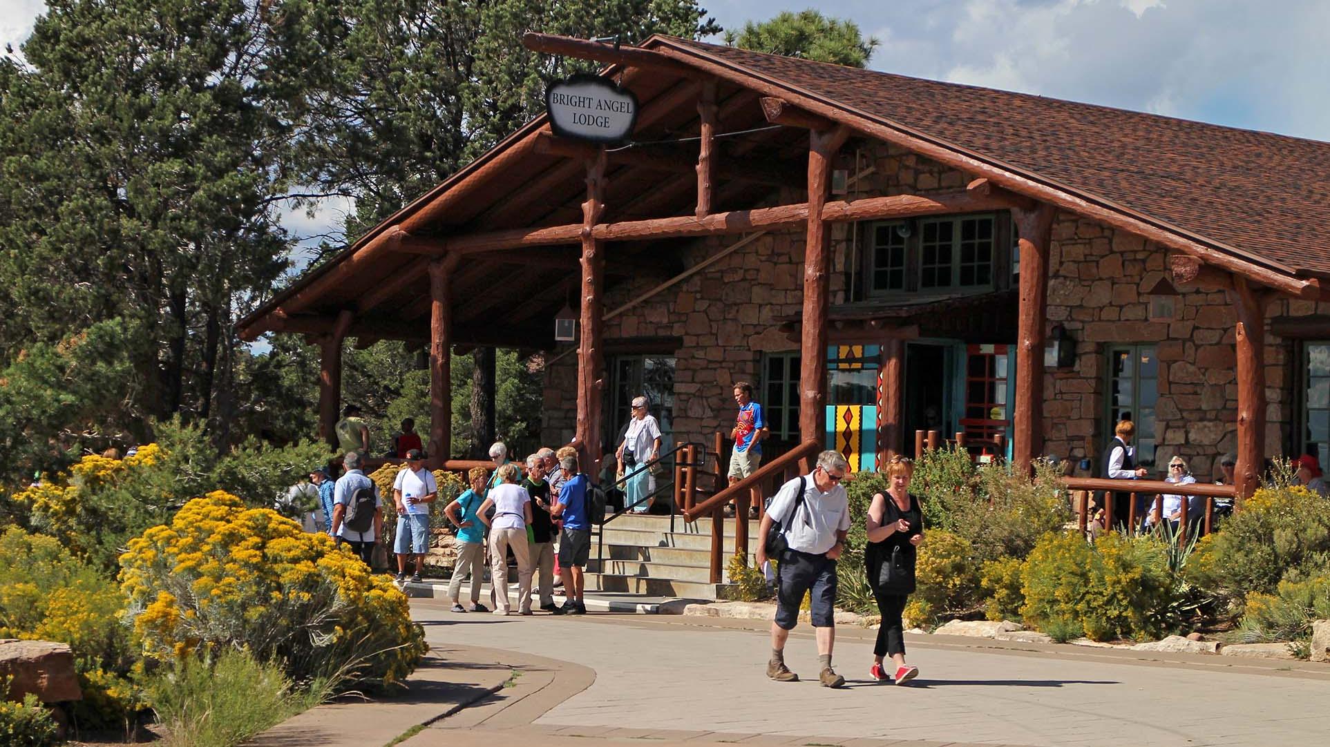 park visitors standing in front of a rustic lodge. vegetation is displaying fall colors. 