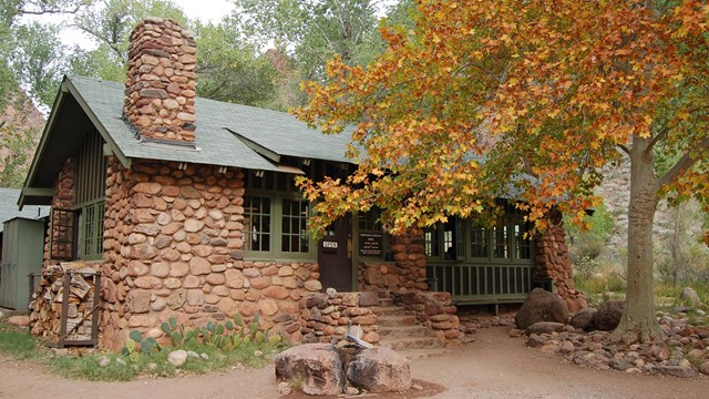 A stone cabin halfway blocked by a tree showing fall leaves.