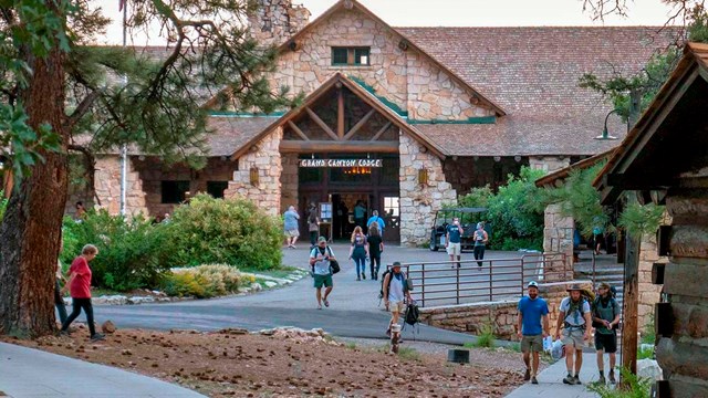 Lodge guests on walkways in front of a rustic stone lodge with a gabled roof above the entrance.