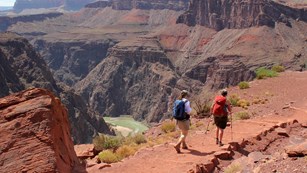 Two hikers walking on a dirt trail. Beyond them the river within a steep granite gorge.