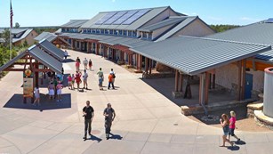 Several people walk through Visitor Center Plaza: outdoor displays on the left, building on right
