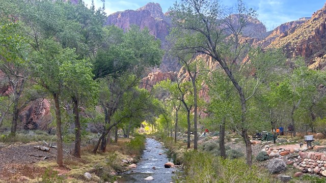 A creek with campsites on one side of the creek and several people with tents