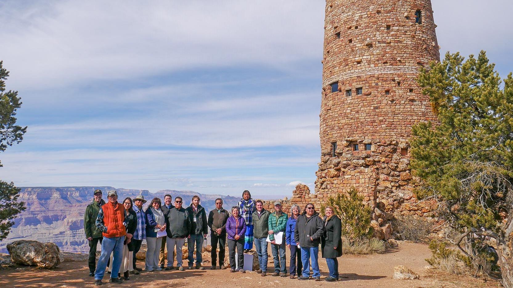 A group of people standing in front of a stone tower with Grand Canyon behind them.