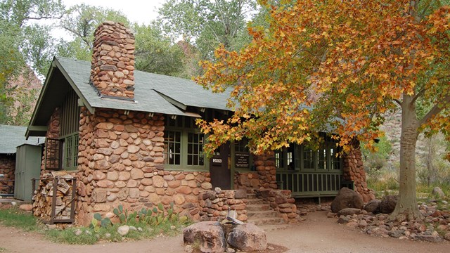 A stone cabin with a tree blocking the front of it.