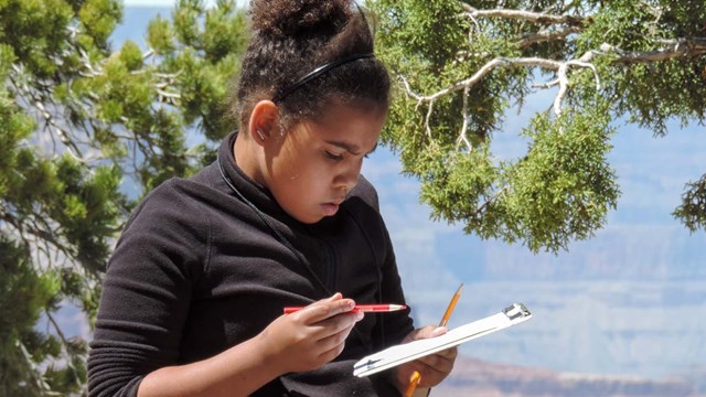 A girl sits on the rim trail working on a booklet