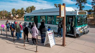 a line of people are waiting in line to board a white and green park bus