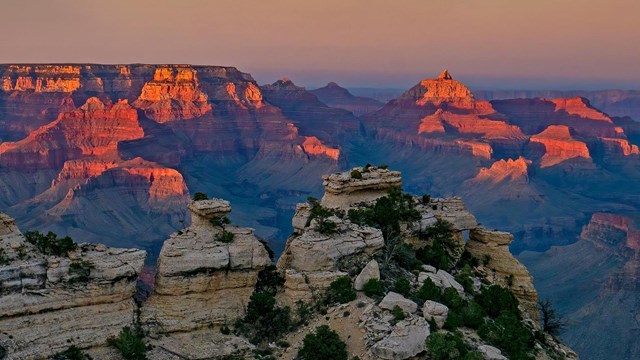 Jagged limestone pillars frame sunset-lit peaks in a vast canyon.
