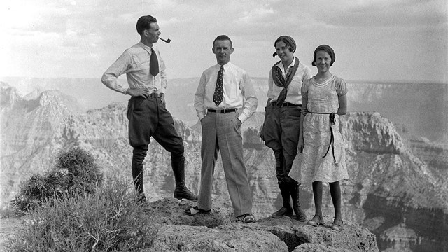 Historic photo of 2 men and 2 women standing on the edge above a large canyon.