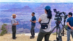 two large videol cameras are recording a park ranger being interviewed by a reporter.
