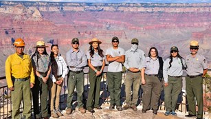 10 indigenous park employees are posing for a group photo in front of the canyon landscape.