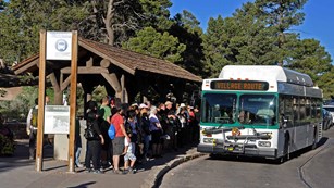 Visitors boarding a park shuttle bus from under a covered bus stop shelter