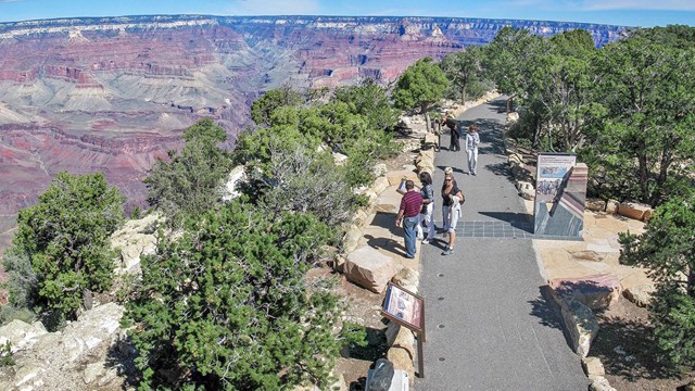 Park Visitors walking on a paved footpath along the edge of a vast and colorful canyon. 