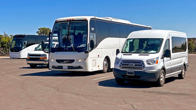 Two large tour buses and two transit vans are parked in a loading zone.