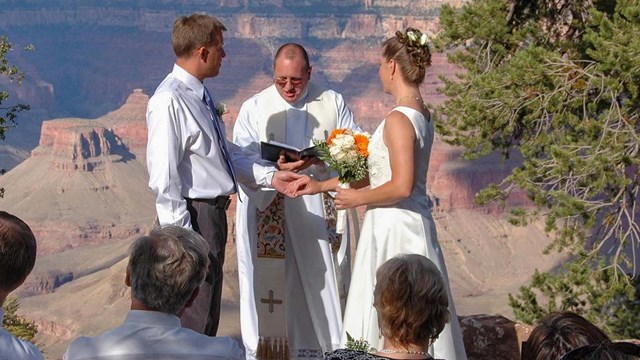 A minister is conducting a wedding ceremony with the couple standing to either side of him.