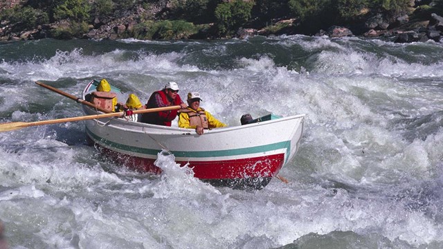 Four people in a wooden dory running a rapid