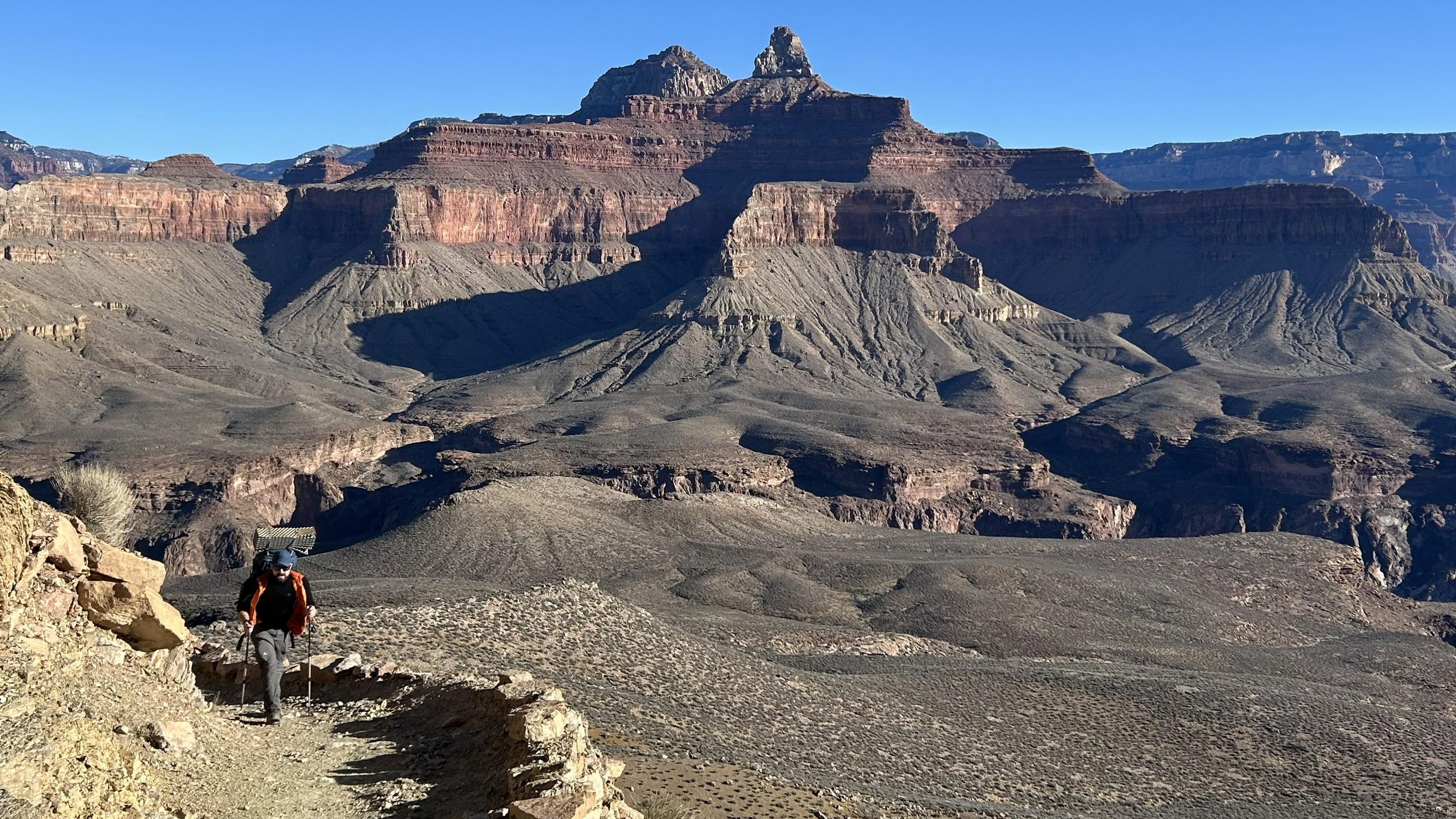 On a backcountry trail a hiker with a backpack walks uphill. 