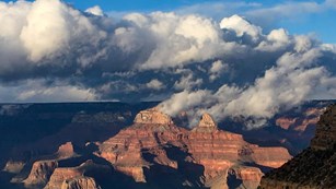 complex patterns formed by storm clouds above a vermilion colored peak within a vast landscape.