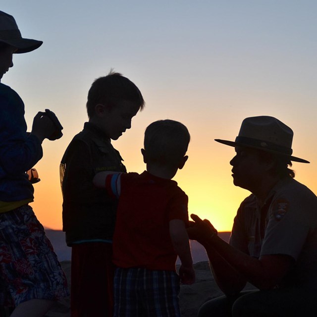 Silhouette of a Park Ranger and students interacting, in front of a stunning Grand Canyon sunset. 