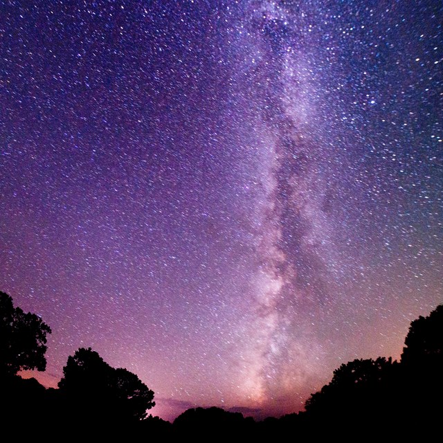 A black to purple gradient sky is illuminated by millions of bright stars.