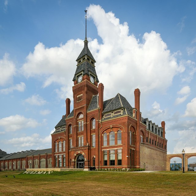 A red bricked four-story tall building with clock tower attached two archways