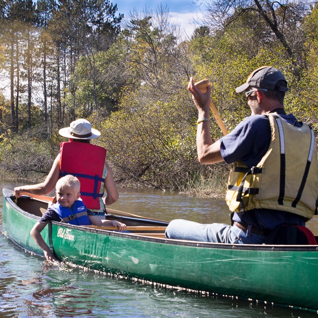 Two adults and a child paddling a canoe on the river