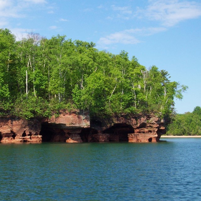 Rock outcrop of Sand Island including waters of Lake Superior and sea caves covered by forest 