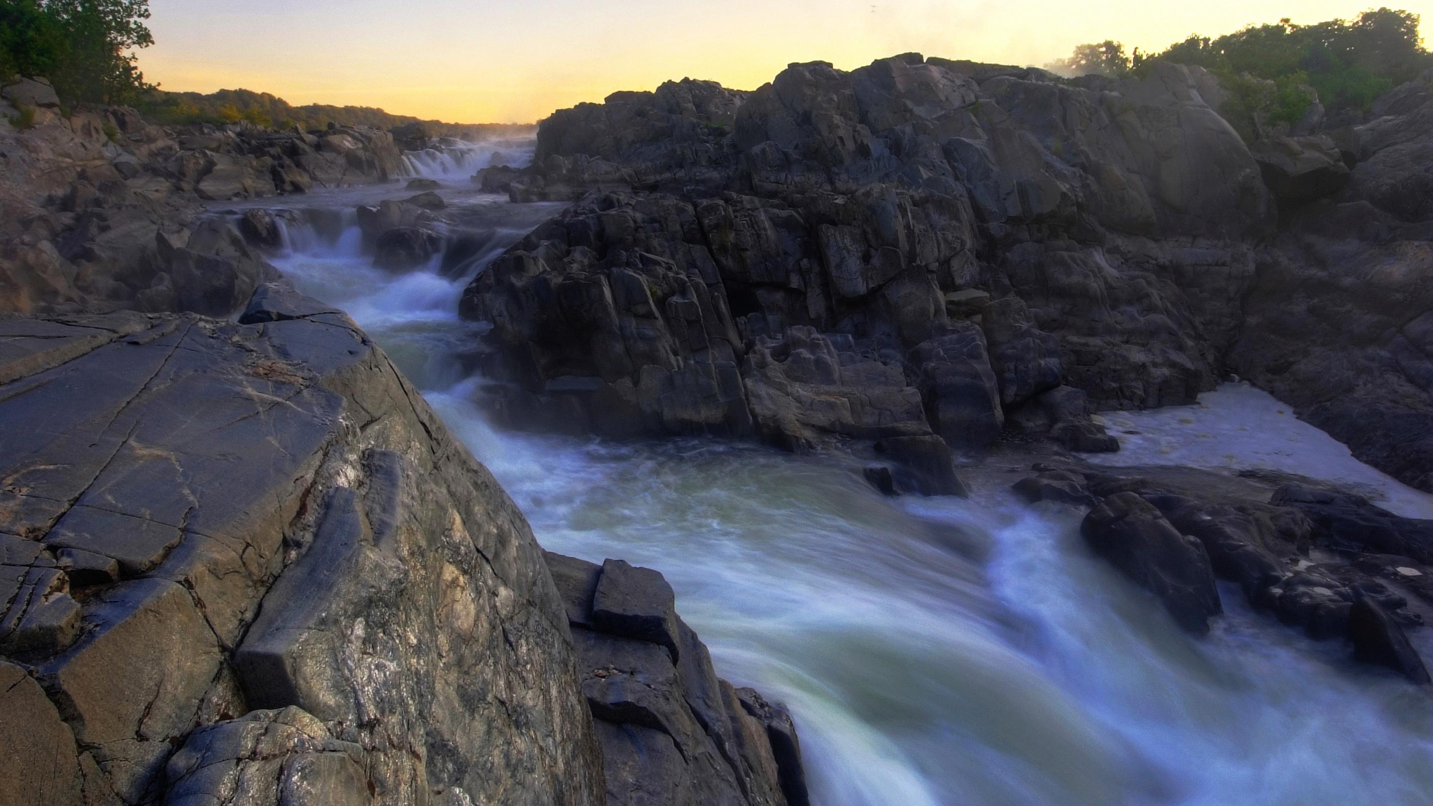 Flowing water over dark rocks at sunrise.