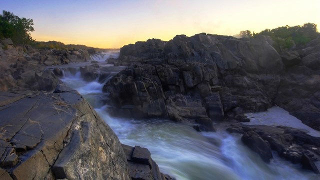 Flowing water over dark rocks at sunrise.