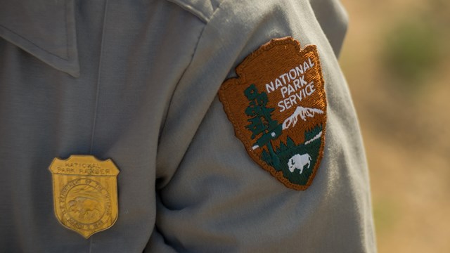 The NPS patch on a grey uniform shirt with a gold badge.