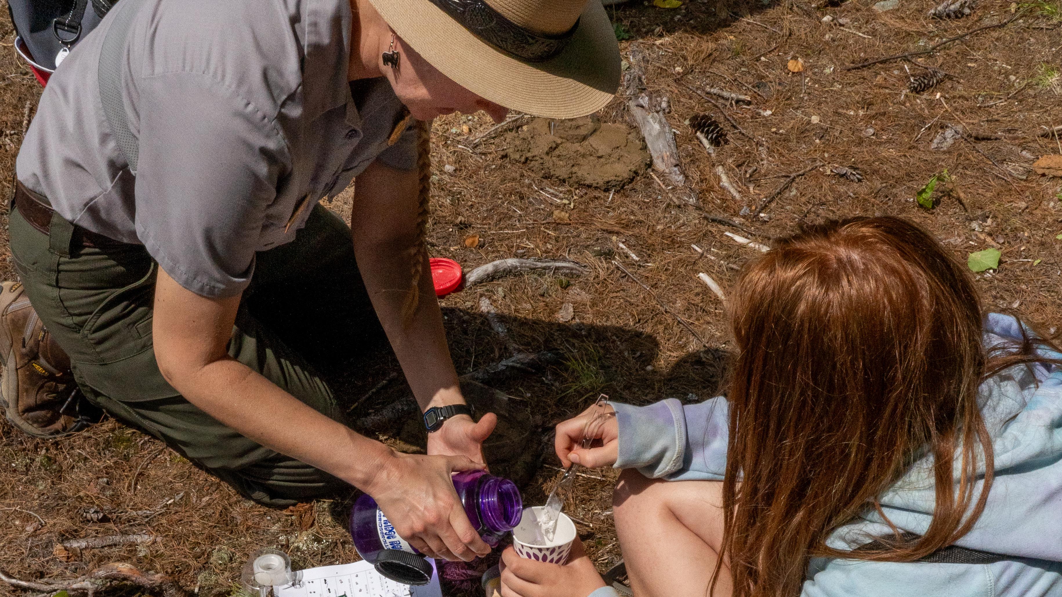A ranger pours liquid into a paper cup of a student's science experiment. 