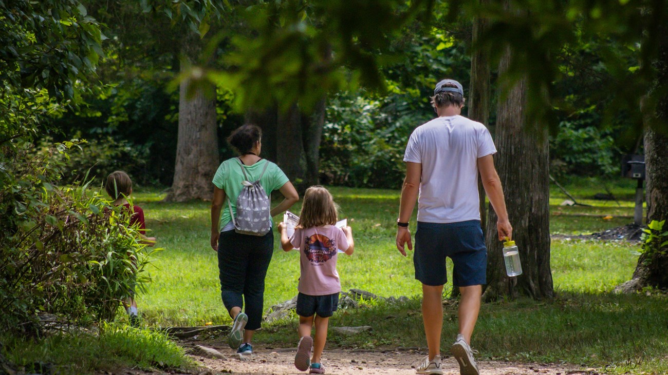 A family of four walks down a trail at Great Falls. A little girl holds open a Junior Ranger booklet