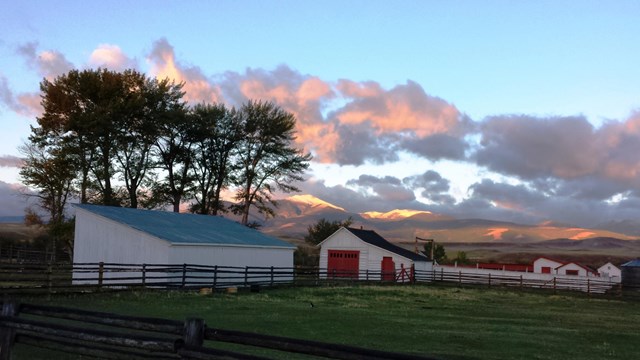 Scenic photo sunrise hits snow-capped mountain in background, white-washed barns