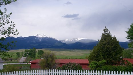 Scenic photo of rain storm over snow-capped mountain in background, red barn, blooming lilacs 
